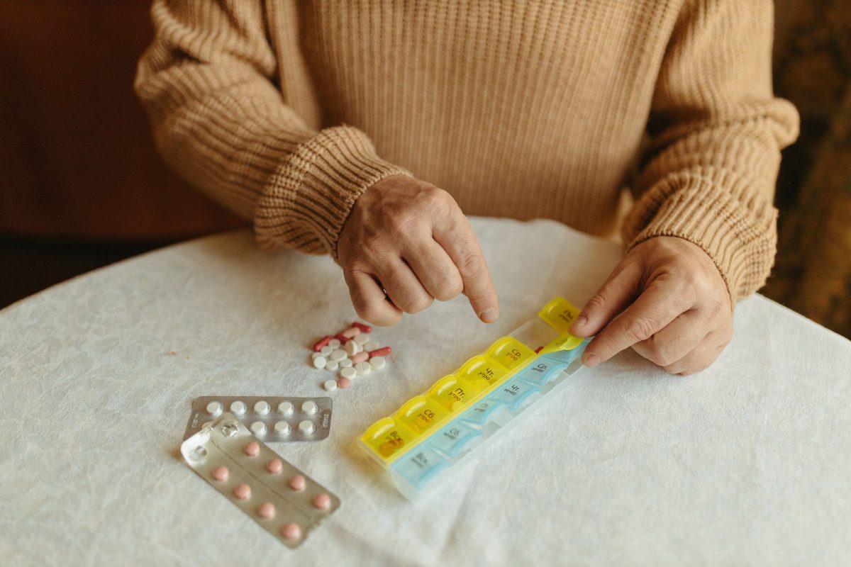 Hands sorting daily medications into a weekly pill organizer