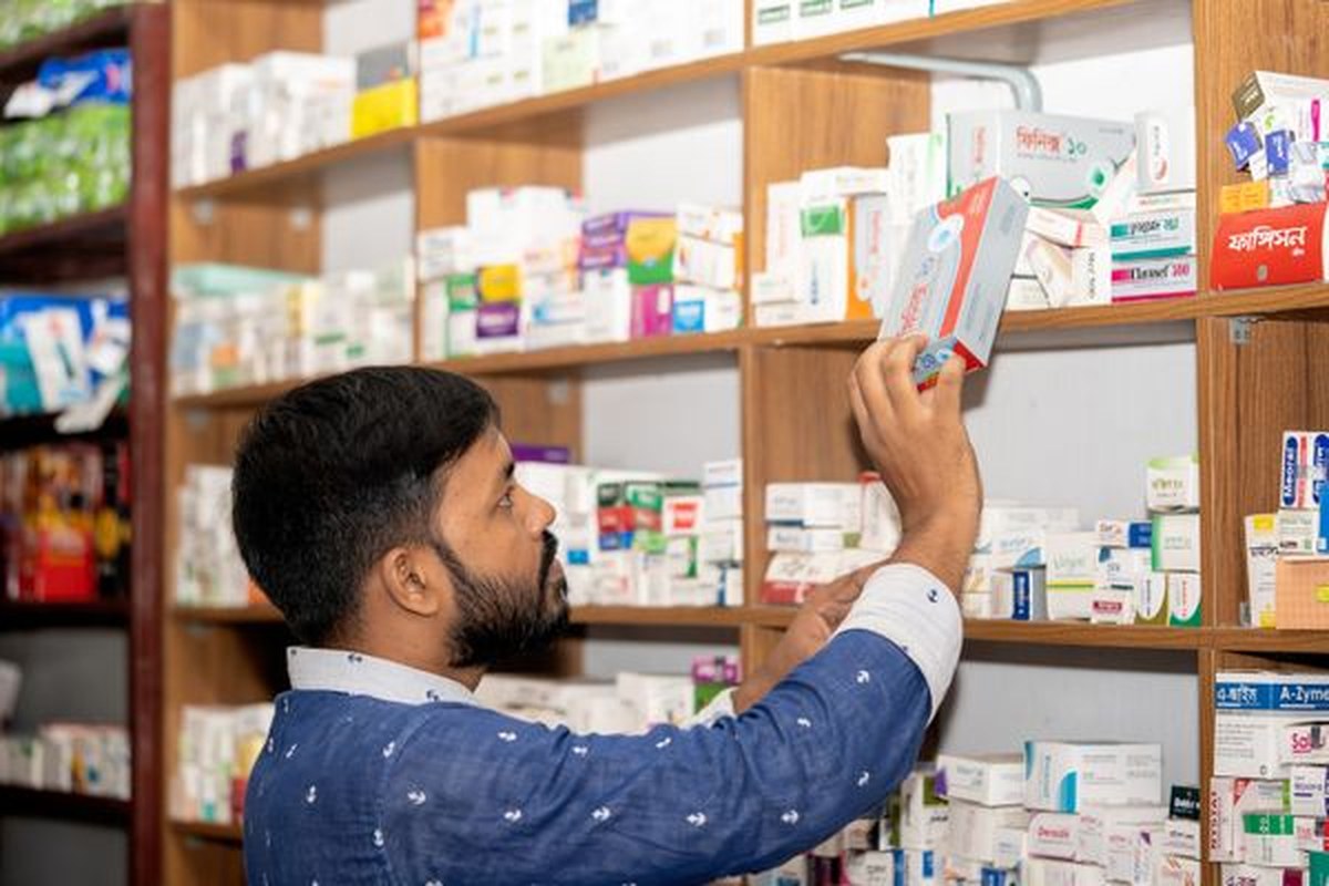 A pharmacist in a white coat selecting a medication from the pharmacy shelves